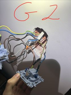 Otwór w ścianie z przewodami i trzymany osprzęt łącznika; na górze czerwony napis „G2”