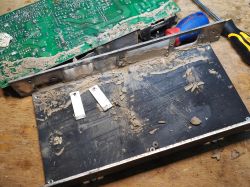 Wnętrze rozebranego switcha pokrytego błotem i kurzem po zalaniu, widoczna płyta PCB oraz obudowa.