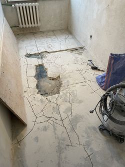 Pokój z pęknięciami w posadzce i odkrytymi miejscami betonowymi.