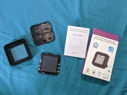 Disassembled S09 IR remote with temperature and humidity sensor, user manual, and original packaging lying on a blue surface.