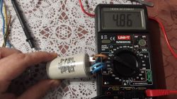 Kondensator trzymany w ręce obok multimetru pokazującego 4,85 µF.