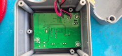 Printed Circuit Board in Plastic Case A green printed circuit board mounted inside a gray plastic enclosure with a few wires connected at the top.