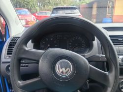 View of a Volkswagen car steering wheel from inside the cabin, with parked cars visible through the windshield.