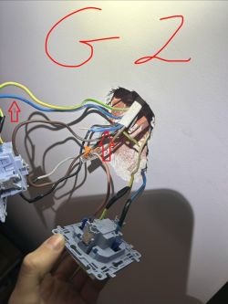 Otwór w ścianie z widocznymi przewodami i trzymanym osprzętem elektrycznym; czerwone strzałki i napis „G2”
