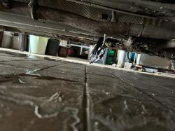 A vehicle's undercarriage with a component hanging on wires.