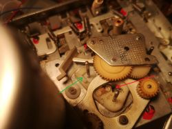Zbliżenie na mechanizm zegara z zaznaczonymi strzałkami miejscami brakującego filcu.