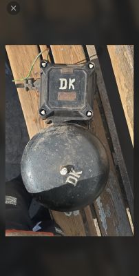 Czarny metalowy dzwon i skrzynka z napisem „DK” na drewnianych deskach