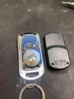 Otwarty pilot do bramy z widoczną płytką elektroniczną i baterią na czarnym tle.