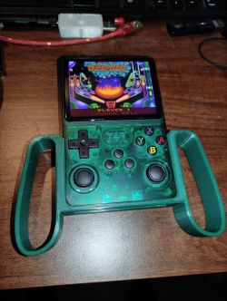 Handheld green gaming console with handle, playing pinball game on screen