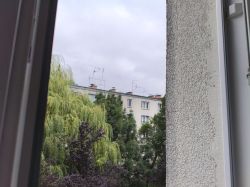 Widok z okna na dachy bloku z daszkami nad kominami i antenami