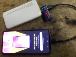 Biały powerbank WPBWE1 z podłączonym amperomierzem i telefonem.