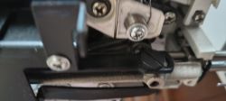 Zbliżenie na mechanizm maszyny z metalowym ramieniem, śrubami i czarną dźwignią zacisku