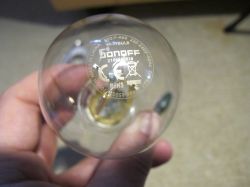 A person holding a transparent Sonoff Wi-Fi bulb with visible technical markings and certifications.