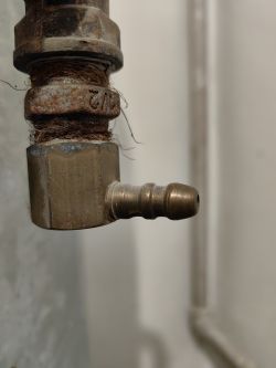 Metalowe złącze kątowe z gwintem i nyplem na tle ściany
