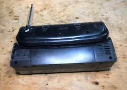 Back and Top View of Portable Radio with Antenna A black, rectangular portable radio on a wooden surface, viewed from the top and back; an extended telescopic antenna is visible.