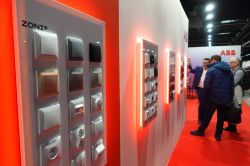 Display panel with ZONI switches and sockets at a trade show booth; people talking in the background