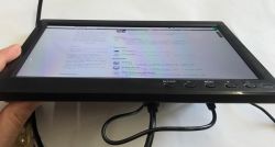 Small black monitor on a desk held by a hand, with a cable connected and a web page displayed on the screen