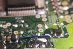 Zbliżenie na płytkę drukowaną z elementami elektronicznymi, rezystorami i niebieskim przewodem.