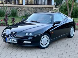 A black Alfa Romeo GTV car parked on a cobblestone surface.
