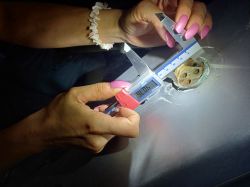 A woman measuring a metal component with calipers.
