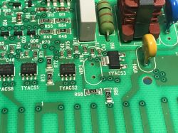 Zbliżenie na fragment płytki drukowanej z widocznymi elementami elektronicznymi, takimi jak triaki ACS1026T, rezystory, cewka i warystor.