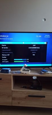 Ekran telewizora z menu ustawień instalacji kanałów DVB-T oraz akcesoria RTV na szafce pod telewizorem.