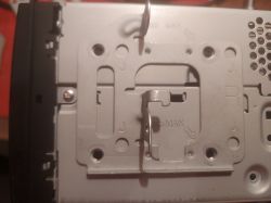 Zbliżenie wnętrza urządzenia elektronicznego z widocznymi metalowymi elementami i otworami montażowymi.