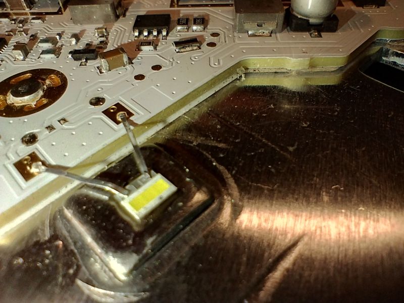 Zbliżenie na płytkę drukowaną z elementami elektronicznymi oraz żółtym chipem LED przylutowanym do podstawy.
