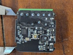 Close-up of a black PCB with a tactile switch and SMD components on a wooden surface
