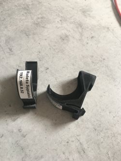 Two black plastic components with a curved shape lying on a concrete surface. One component has a label with text.