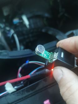 Osoba trzyma mały obwód drukowany z przylutowanym mikrofonem, w tle widoczne są przewody.