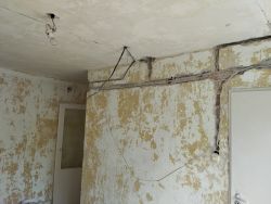 Ściana i sufit w trakcie generalnego remontu z widoczną starą żarówką i kablami.