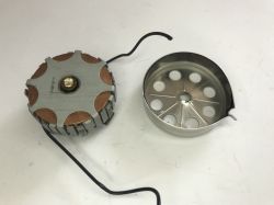 Two metal mechanism parts on a white surface, connected by a black wire