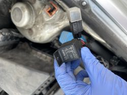 Osoba w rękawiczkach trzyma przekaźnik samochodowy pod maską.