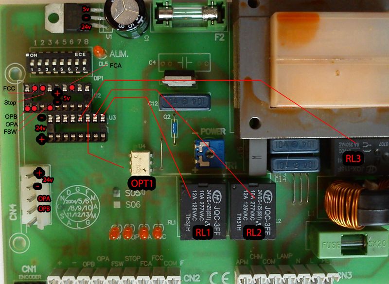 Płyta główna centralki z oznaczonymi pinami i napięciami, elementy elektroniczne podpisane na czerwono.