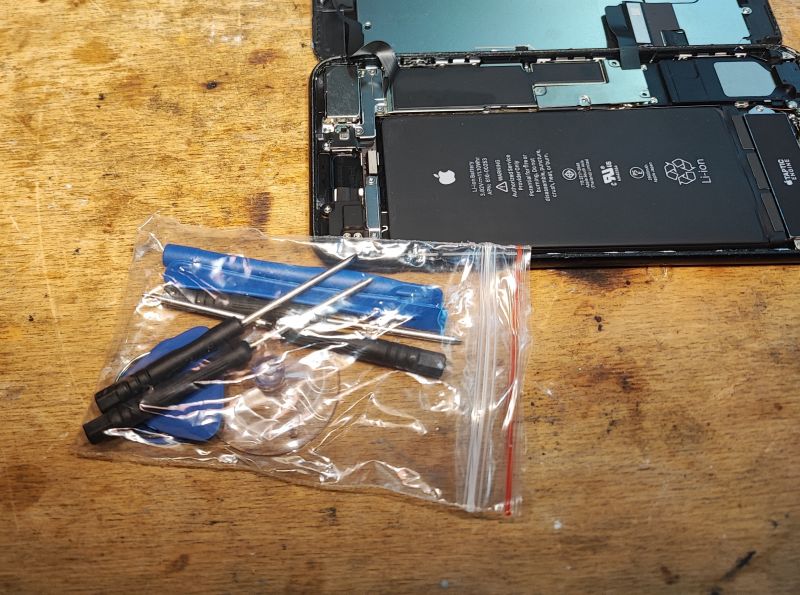 Battery Replacement Tool Kit for iPhone Battery replacement tools and an open iPhone on a wooden table.