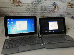 Dwa laptopy HP Mini 210 stojące obok siebie na tle kolorowej ściany z graffiti, oba mają otwarte ekrany z uruchomionym programem CPU-Z.