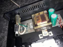 Wnętrze urządzenia elektronicznego z widocznym transformatorem i kondensatorami.