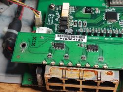 Zbliżenie na płytę główną switcha sieciowego z widoczną korozją na złączach portów Ethernet i modułem LED.