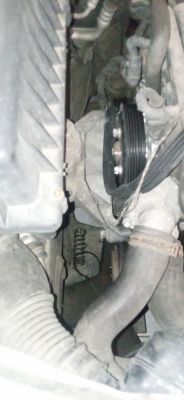 Widok komory silnika Opel Astra H z widocznym kołem pasowym i wystającą sprężyną.