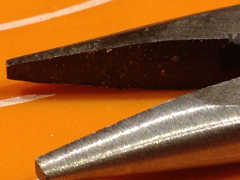 Zbliżenie na końcówki dwóch rodzajów kombinerek na pomarańczowym tle.