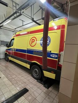 Ambulans w garażu serwisowym z podłączonym wężem.