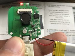 Close-up of a printed circuit board with electronics and a camera, held between fingers.