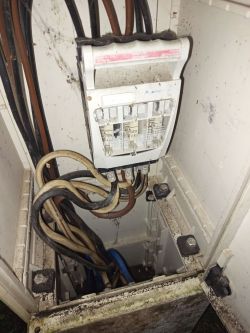 Widok wnętrza skrzynki elektrycznej z przewodami i bezpiecznikami.