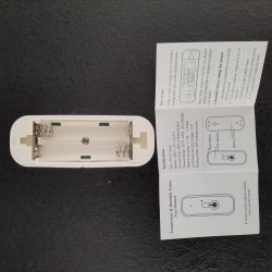 Temperature and humidity sensor with an open battery compartment and a user manual on a black surface.