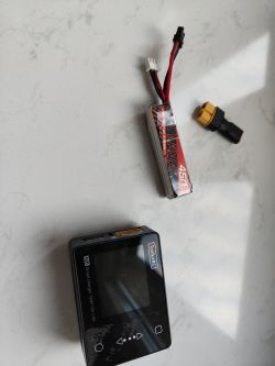 Bateria LiPo, ładowarka ToolkitRC oraz adapter XT60 leżące na stole.