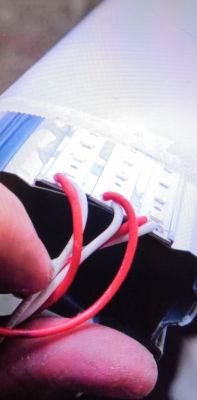 Zbliżenie na rękę trzymającą przewody przy elemencie elektrycznym z listwy LED.