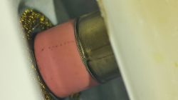 Zbliżenie na różowy ceramiczny element z metalowym pierścieniem, otoczony złotymi opiłkami.