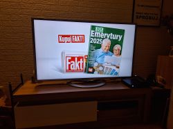 Telewizor wyświetlający reklamę gazety Fakt na drewnianym stoliku.