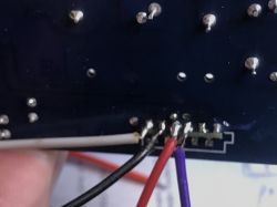 Soldered wires on the garage door controller PCB Close-up of the bottom side of a PCB with four soldered wires: white, black, red, and purple.